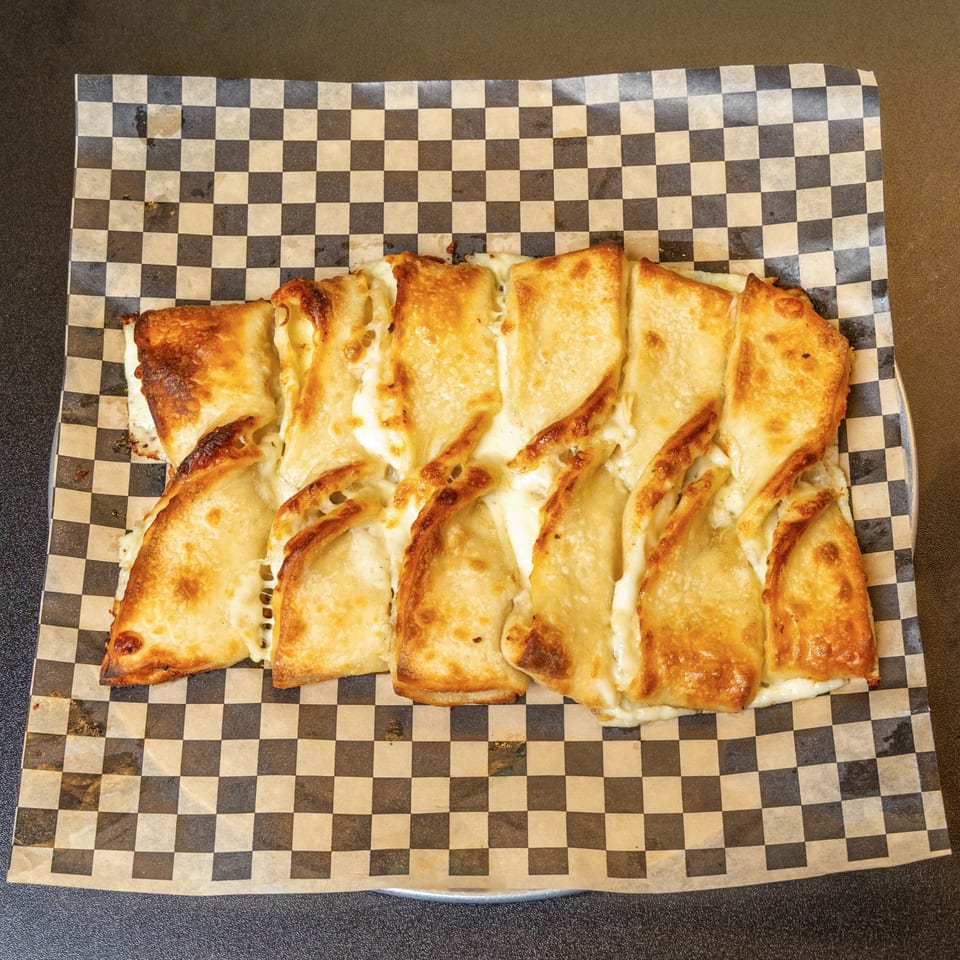 Cheesy breadsticks with melted mozzarella, served on black and white checkered paper.