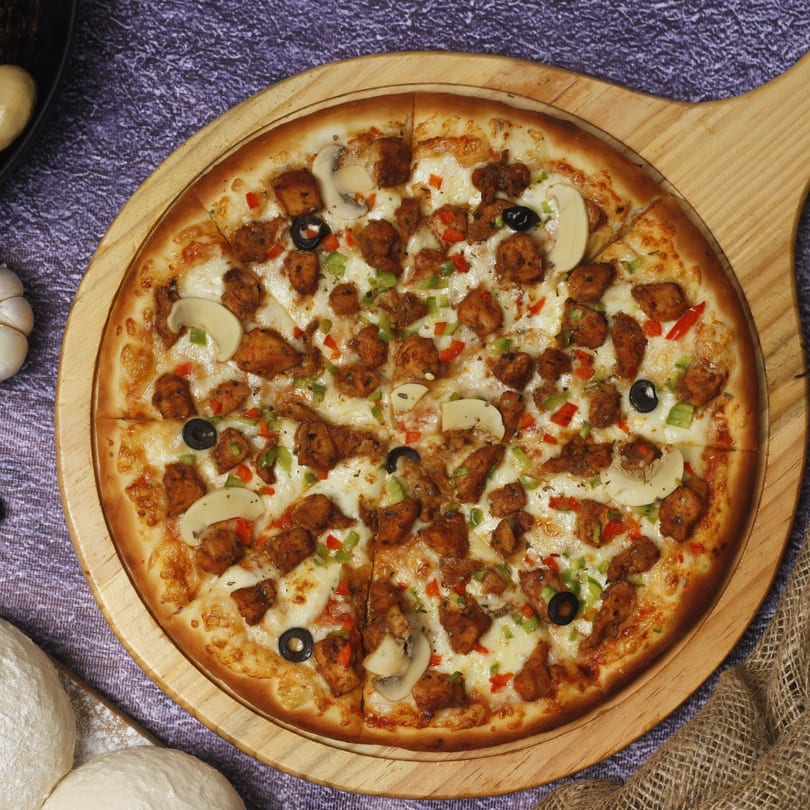 Chicken pizza with mushrooms, olives, and bell peppers on a wooden board.